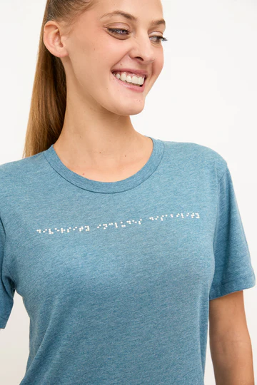 Woman wears light blue t shirt with braille in white across the chest